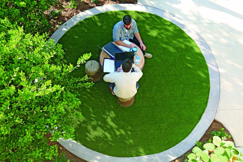 An aerial view of two people at a wooden table and stools working on their laptops together.