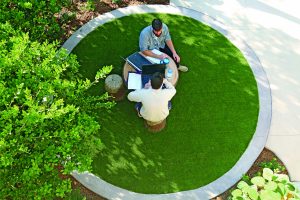 An aerial view of two people at a wooden table and stools working on their laptops together.
