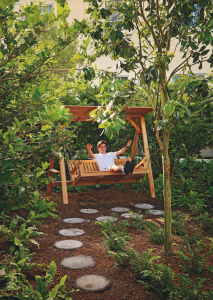 A young person sits on a swinging bench, smiling with their hands waving with joy in the air.