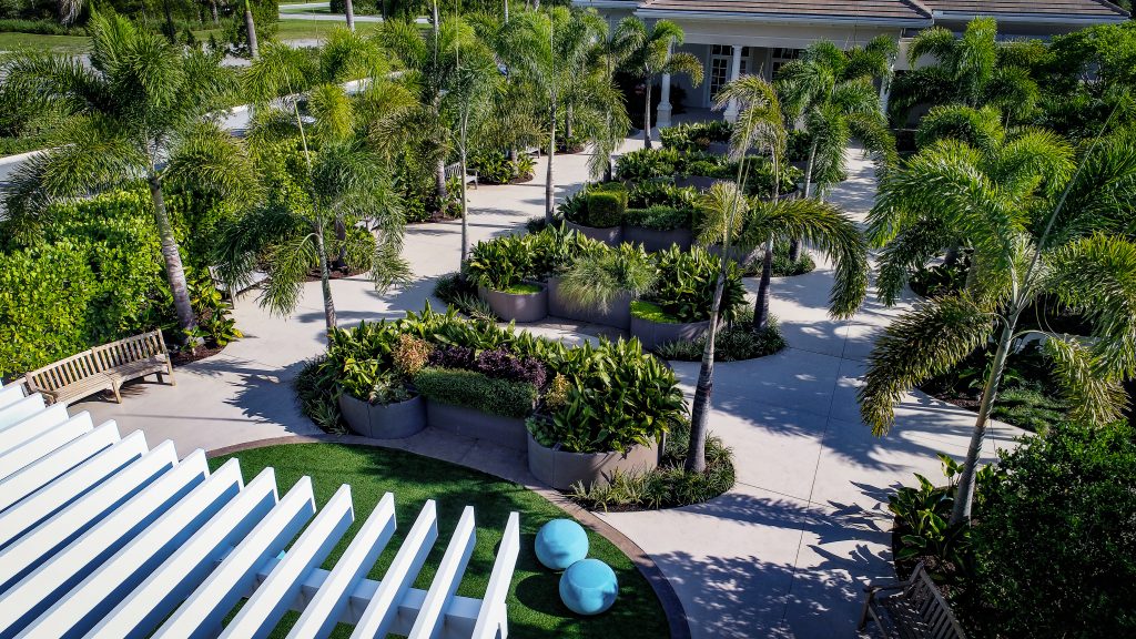 An overview of the garden from above the pergola. A spacious curved trellis serves as a welcoming transition from the elementary school to the garden. The adjacent activity space, an oval “lawn” of resilient paving, features a variety of fixed and movable seating choices.